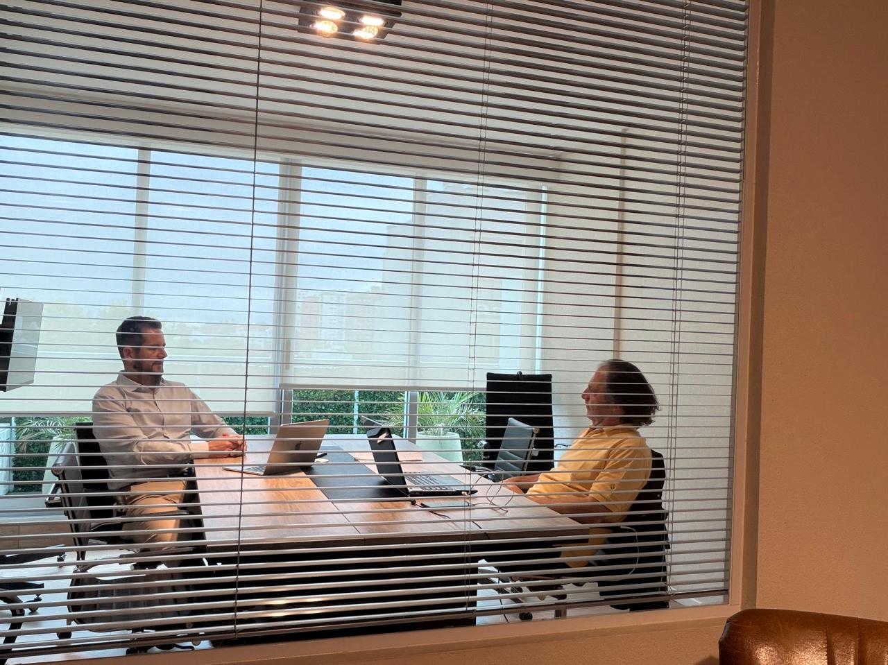 Dos personas conversan frente a sus computadoras en una sala de reuniones.